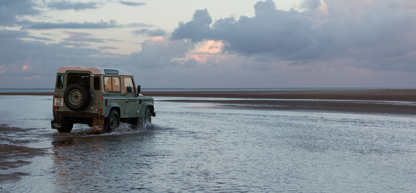 Classic Green Defender 90 driving along the seafront